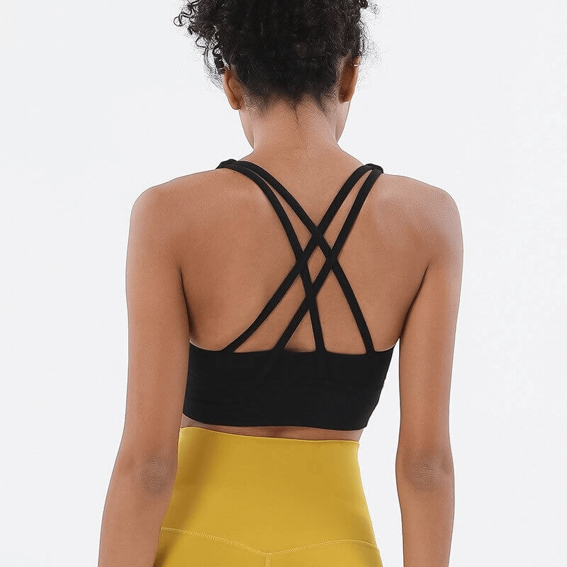 Back view of a woman wearing a black nylon sports top with cross shoulder straps, paired with yellow leggings for fitness.